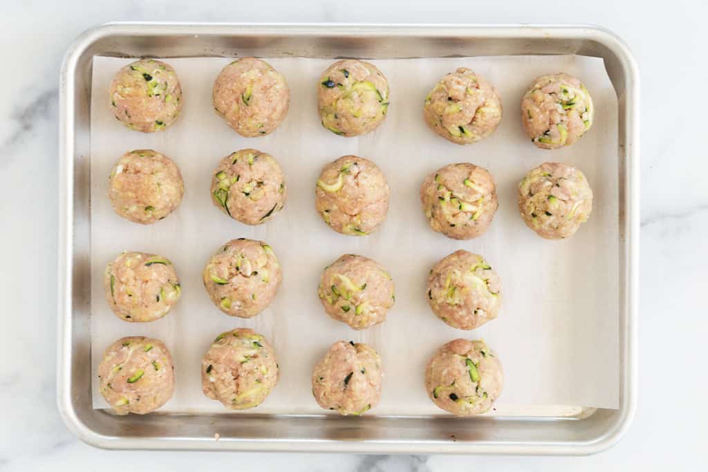 Turkey meatballs with zucchini on baking sheet before baking.