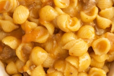 Hands holding bowl of cheeseburger pasta.