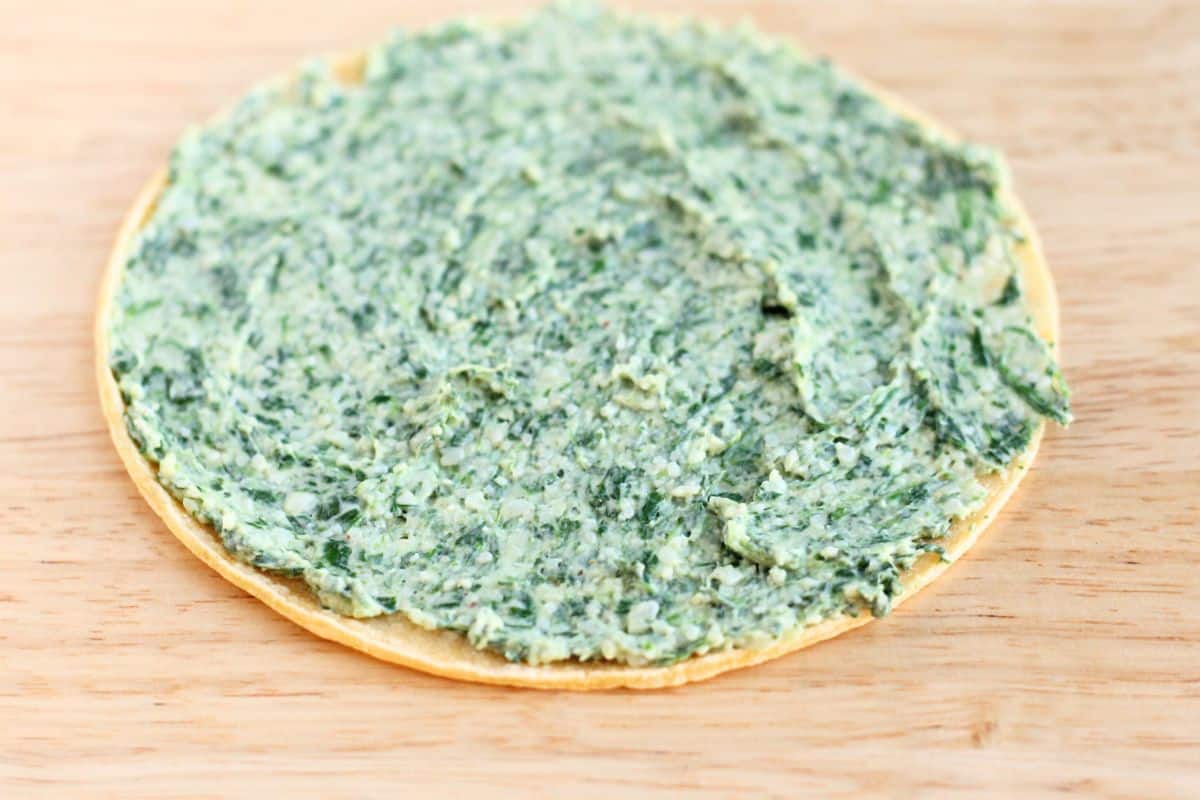 Spinach quesadilla with filling spread on tortilla.