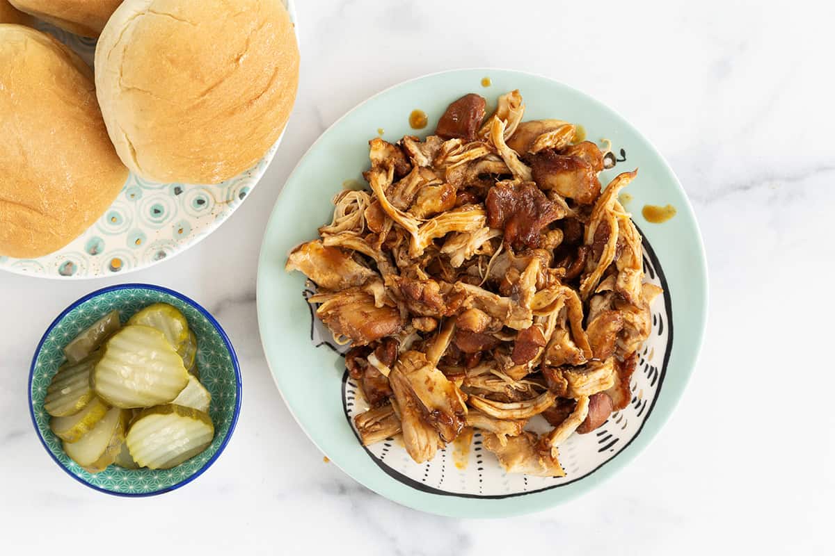 shredded instant pot bbq chicken on plate with rolls and pickles.
