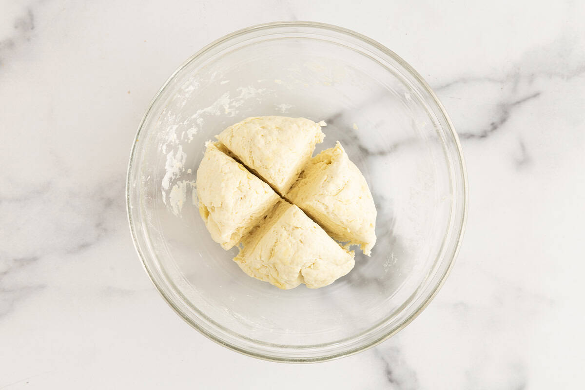 Yogurt flatbread dough in glass bowl divided into 4 pieces.