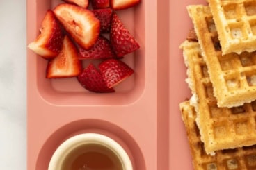 Whole wheat waffles on pink kids plate with strawberries and syrup.
