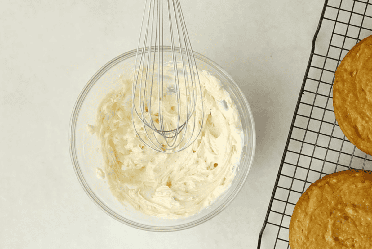 Cream cheese frosting in glass bowl with whisk.