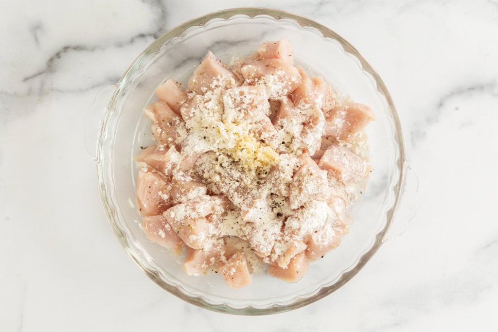 Chicken cubes and seasonings in glass bowl for chicken bites.