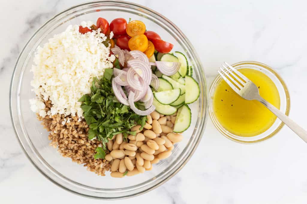 Farro salad ingredients in glass bowl before mixing.