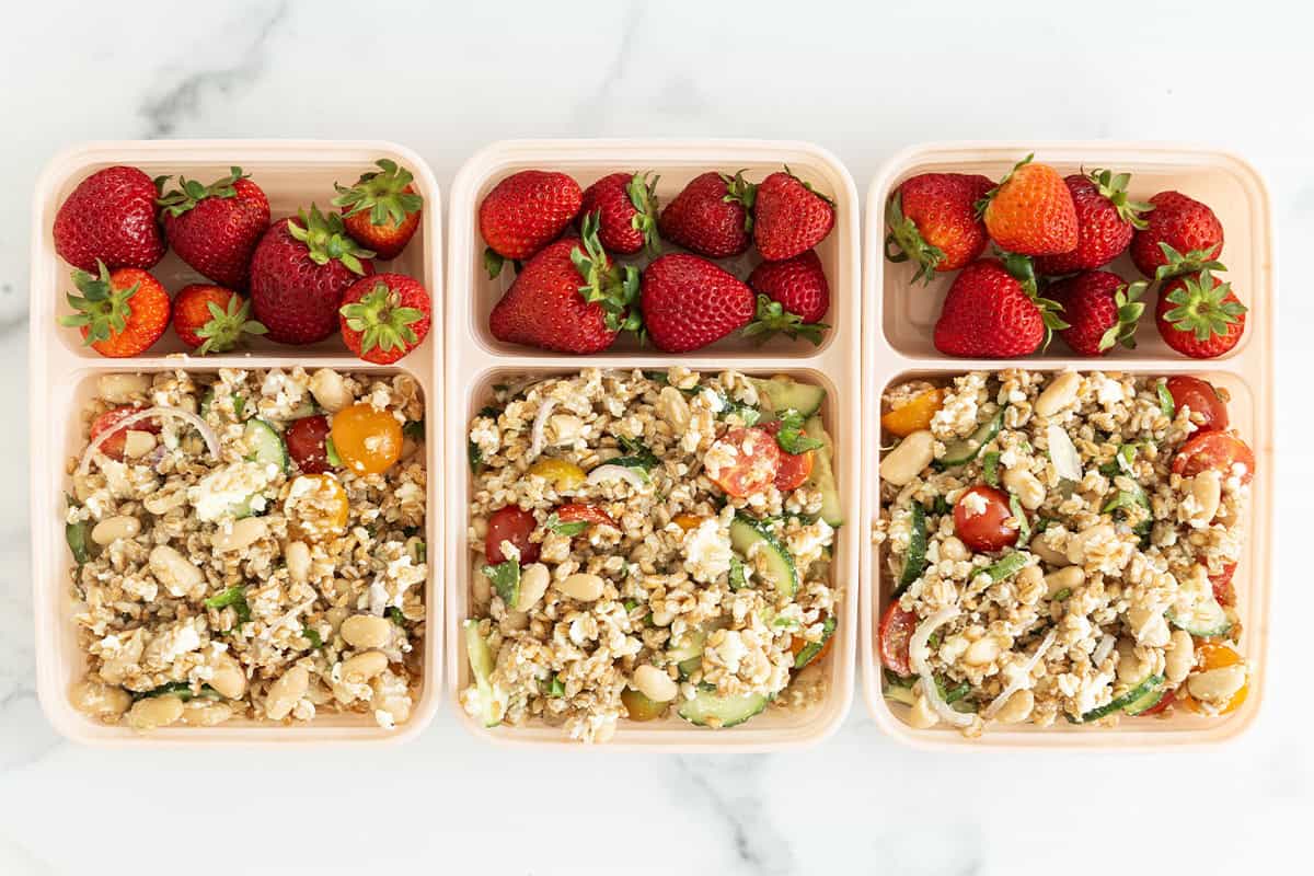 Farro salad in three lunch containers with strawberries.