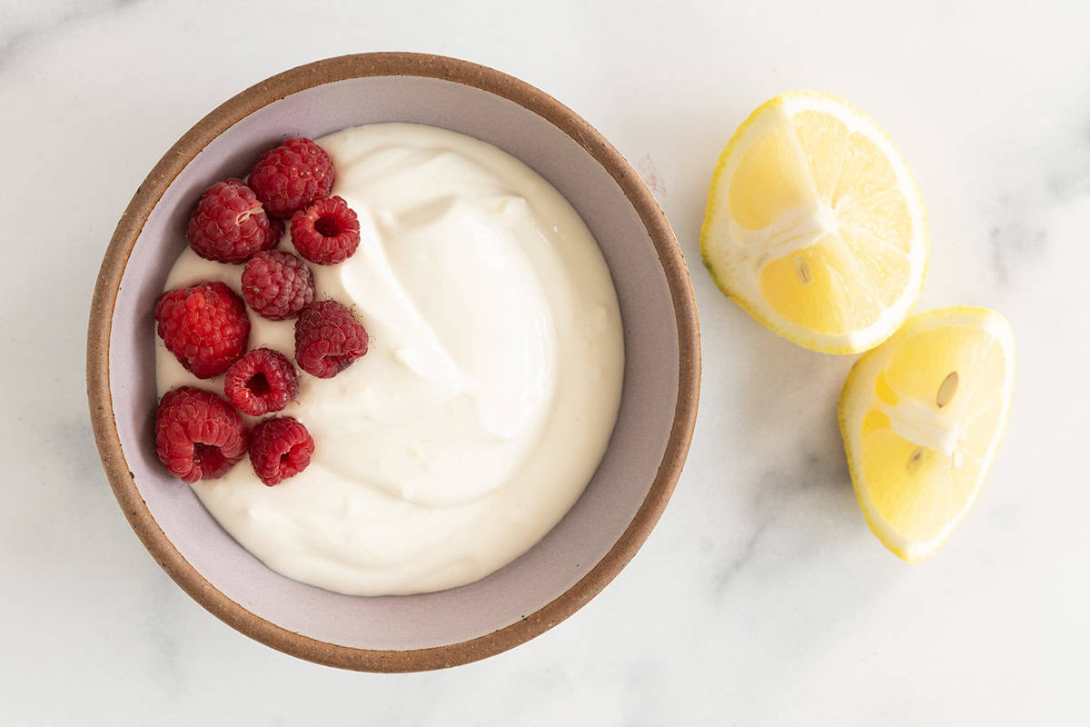 Lemon yogurt in bowl with raspberries.