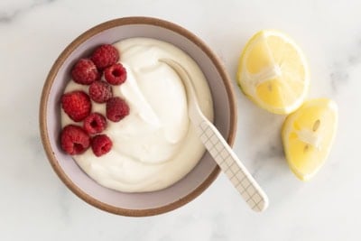 Lemon yogurt in bowl with raspberries and spoon.