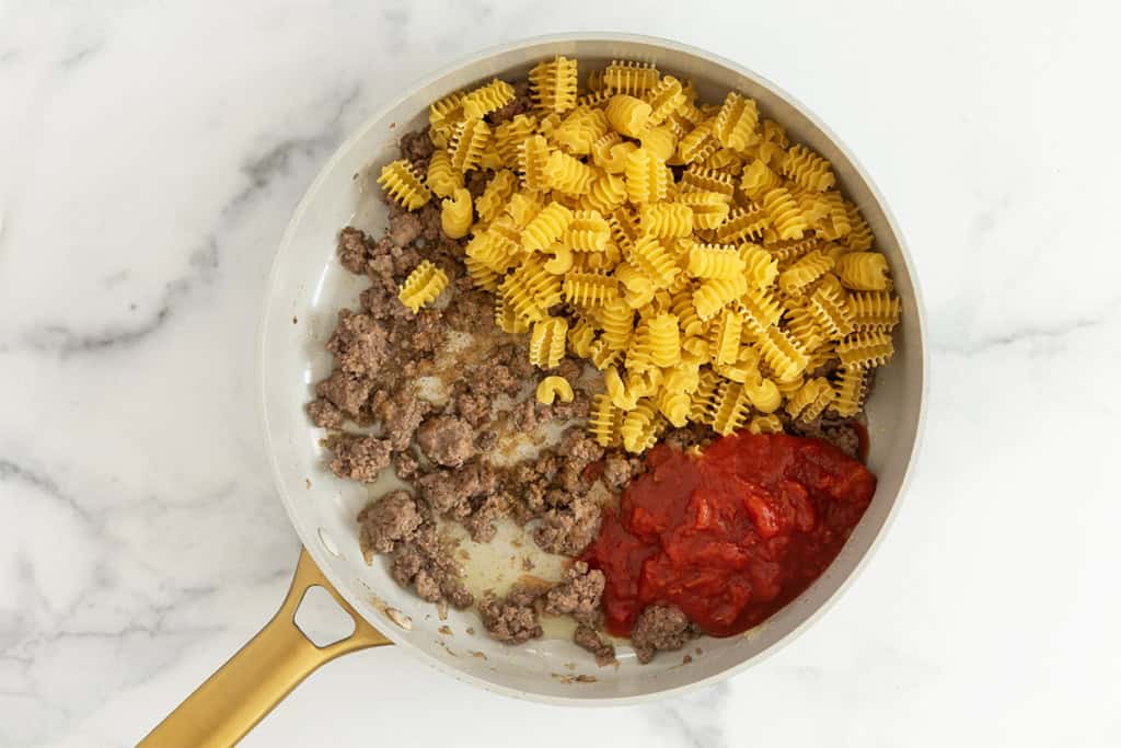 Noodles, beef and tomatoes in pan for taco pasta.