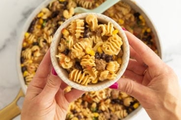 Hands holding bowl of taco pasta.