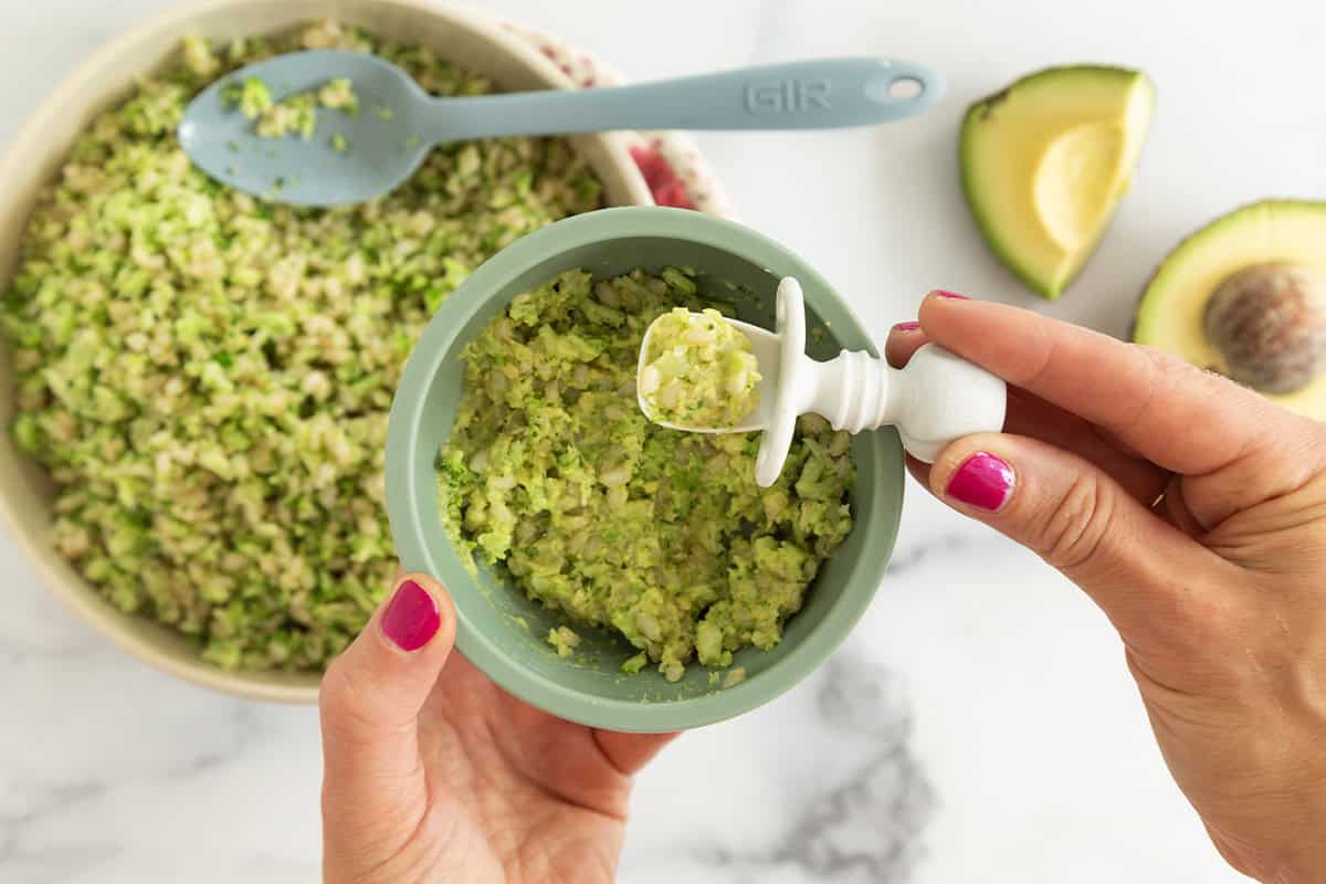 Hands holding broccoli rice in kids bowl.