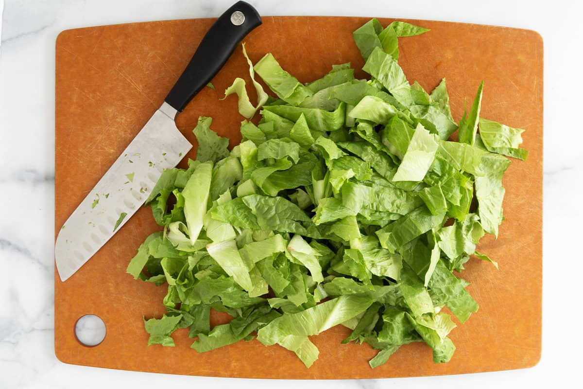 Lettuce cut on cutting board for chicken caesar pasta salad.