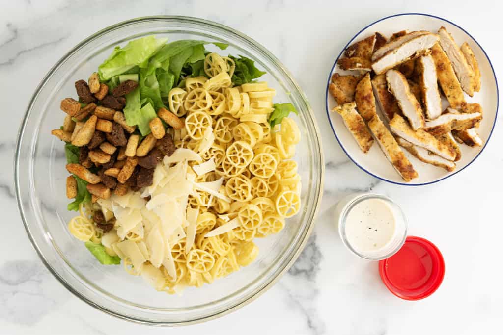 chicken caesar pasta salad in glass bowl with chicken on side.