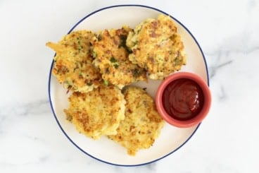 Chicken fritters on white plate with ketchup.