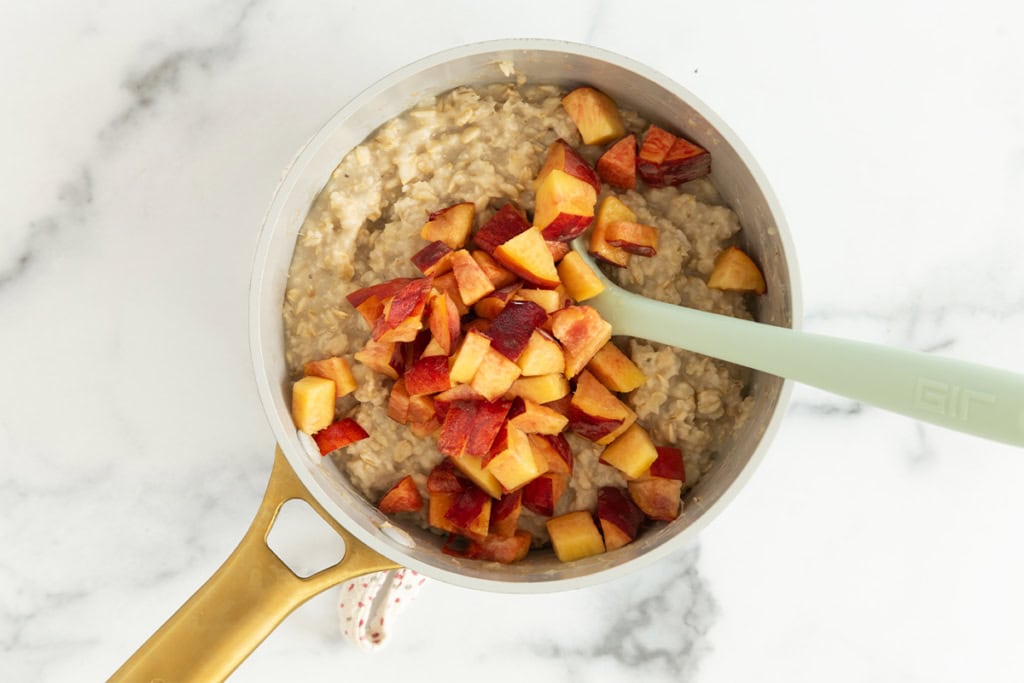 Peaches being stirred into oatmeal in pot.