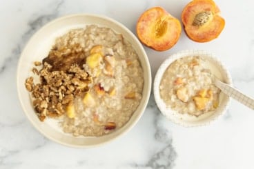 Peaches and cream oatmeal in two bowls with peaches on side.