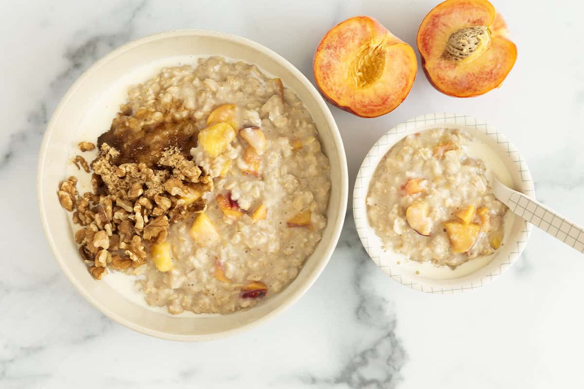 Peaches and cream oatmeal in two bowls with peaches on side. 