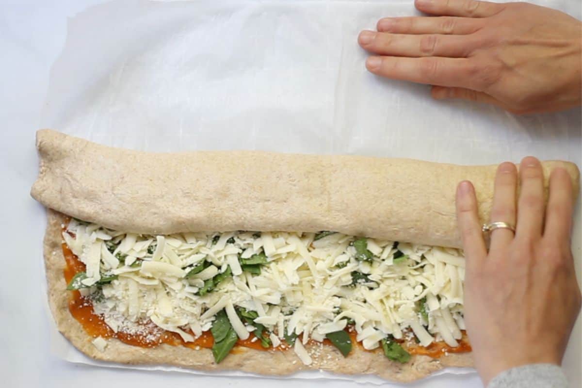 Rolling filled pizza dough into a log for pizza rolls.