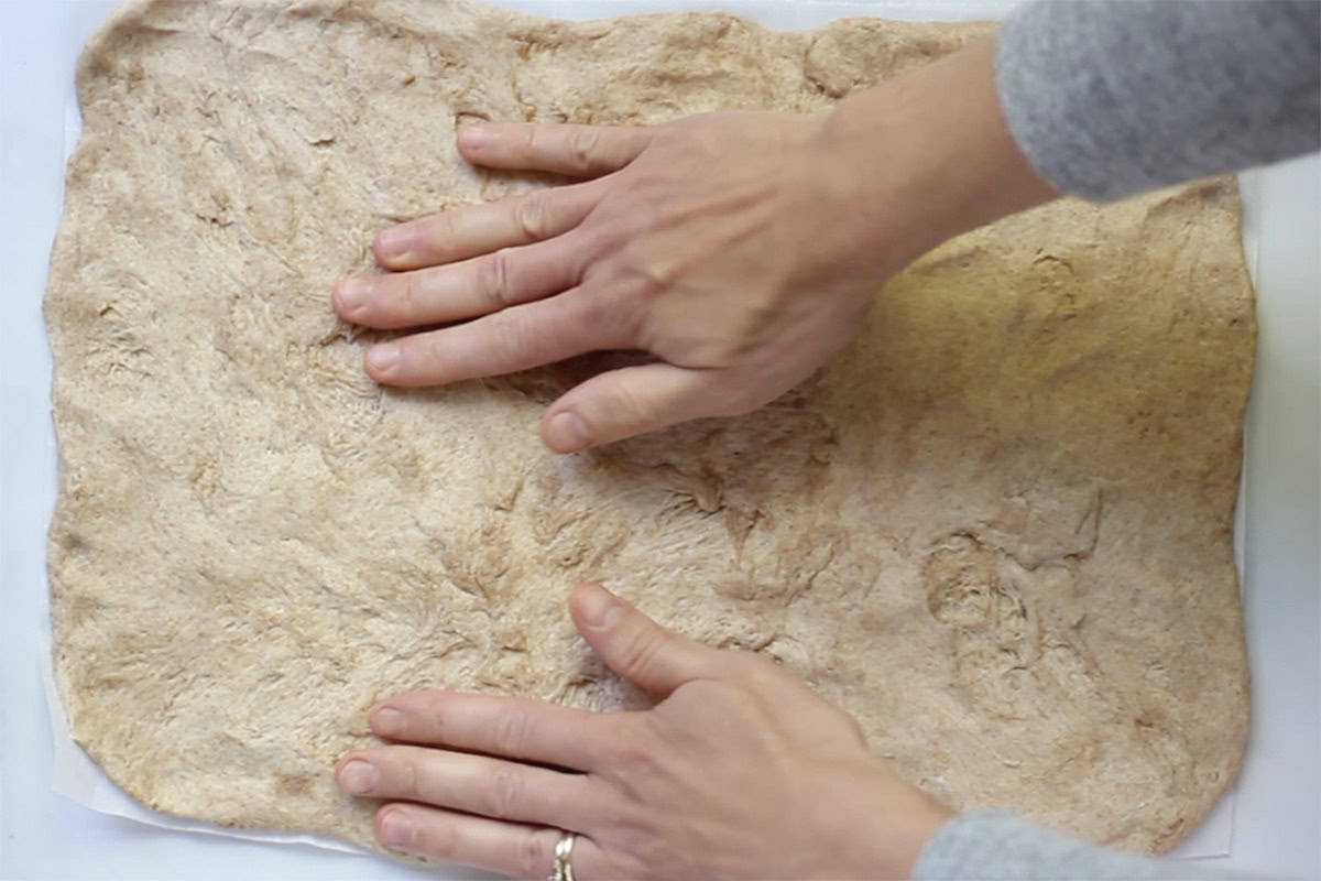 Hands spreading out pizza dough for pizza rolls.