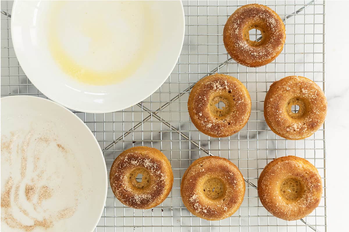 Baked donut dipped in cinnamon sugar on cooling rack.