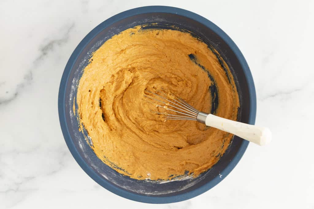 Batter for pumpkin cake in blue bowl with whisk.