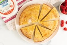 Greek yogurt cake on white plate cut into slices with yogurt container on side.