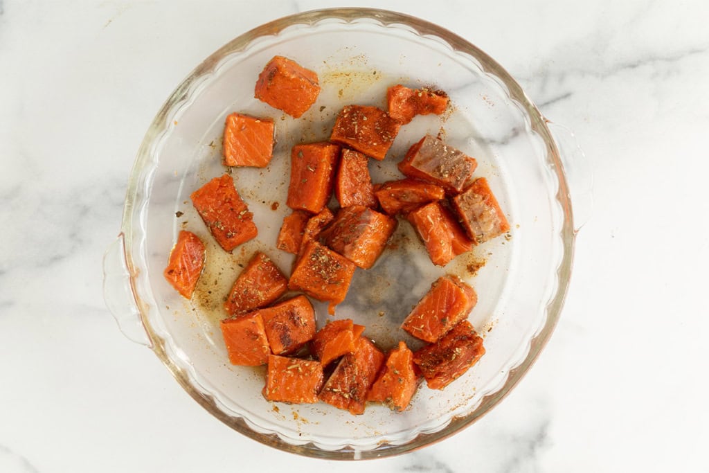 Salmon bites with seasoning in dish before cooking.