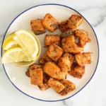 Salmon bites on plate with lemon on side.