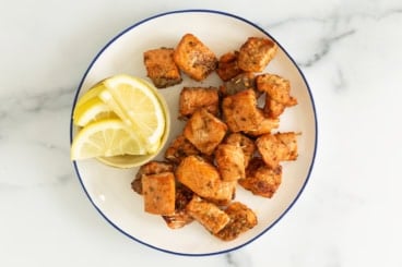 Salmon bites on plate with lemon on side.