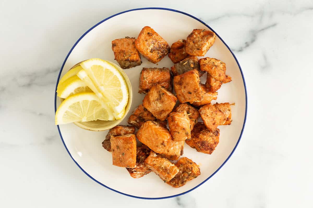 Salmon bites on plate with lemon on side. 