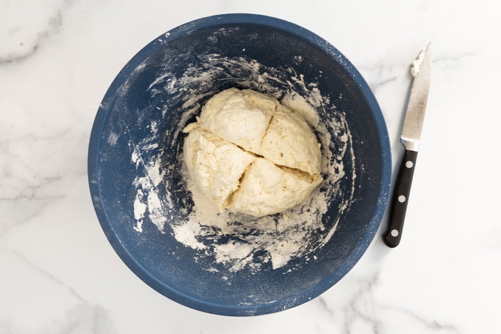 Dough for bagels in blue bowl divided into four.