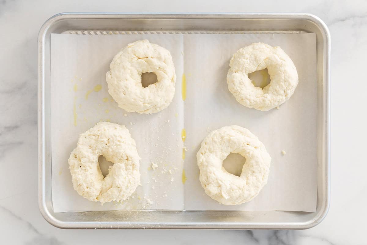 Four bagels on baking sheet before baking.