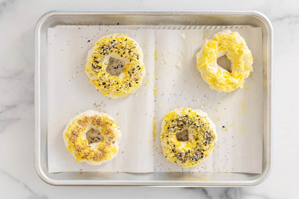 Four bagels spread with seasonings before baking.