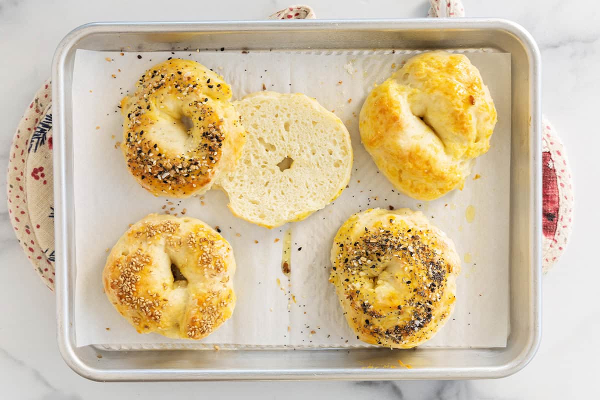 Bagels on baking sheet with one cut open.