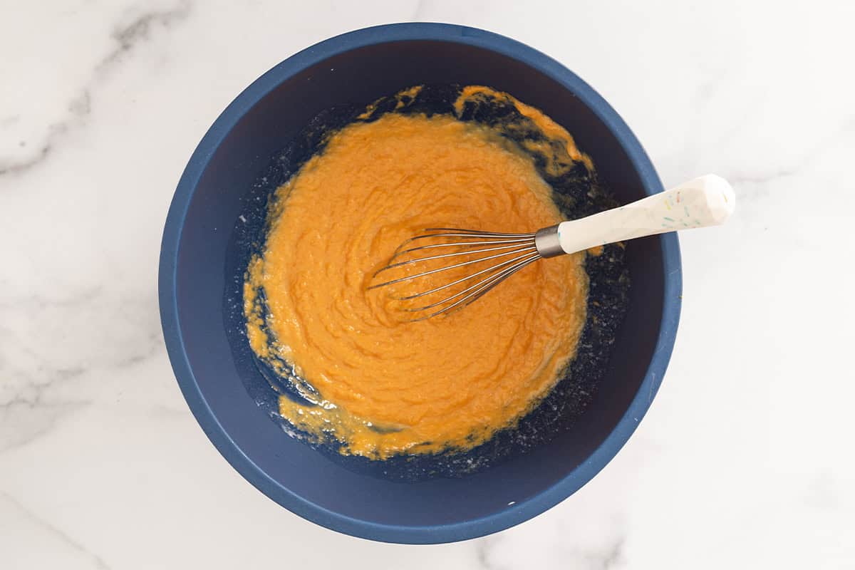 Wet ingredients for baked pumpkin donuts in blue bowl with whisk.