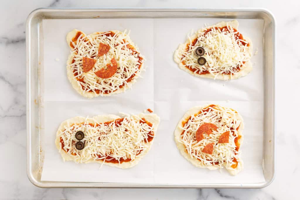 Halloween pizzas on baking sheet before baking.