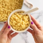 Hands holding bowl of mac and cheese over pan.