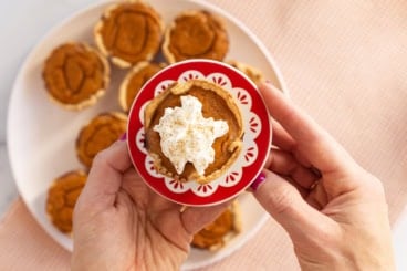 Mini pumpkin pie on red plate with whipped cream.