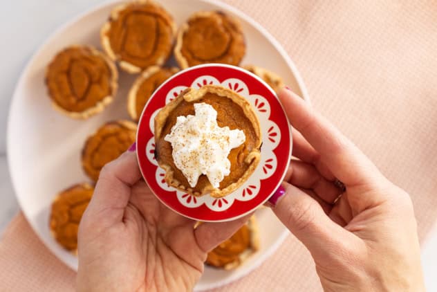 Mini pumpkin pie on red plate with whipped cream.