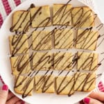 Banana blondies cut into squares and drizzled with chocolate on white plate.