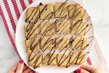 Banana blondies cut into squares and drizzled with chocolate on white plate.