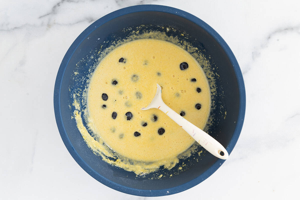 Batter for cornmeal pancakes in bowl with blueberries.