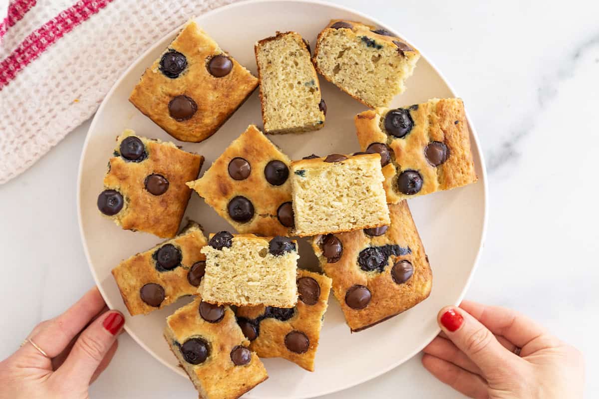 Snack cake slices stacked on white plate with hands holding plate. 