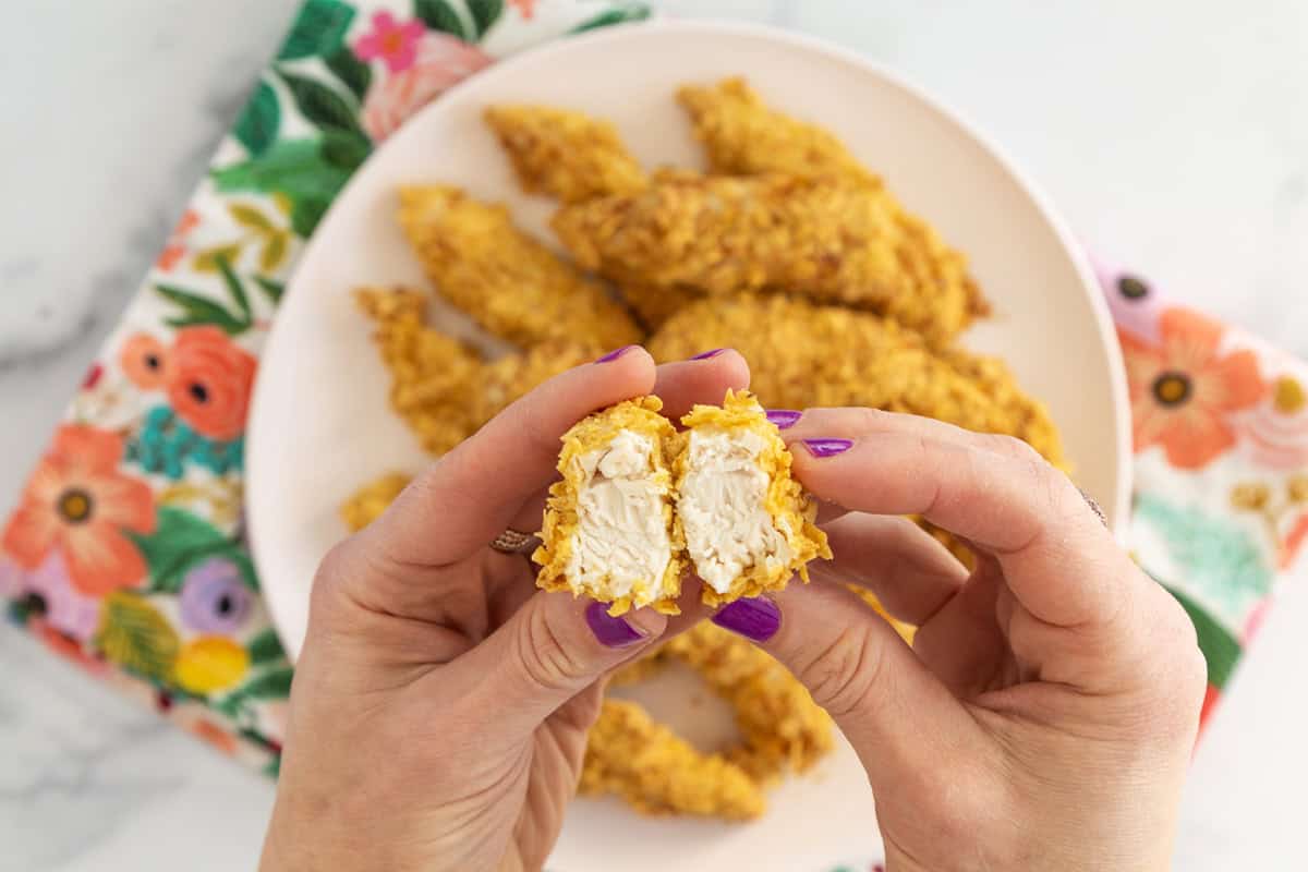 Air fryer chicken on white plate with hands holding strip.