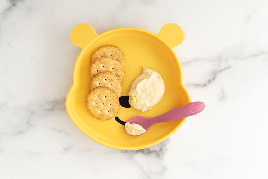 Baby hummus on plate with spoon and crackers.