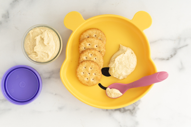 Baby hummus on plate with spoon and crackers.