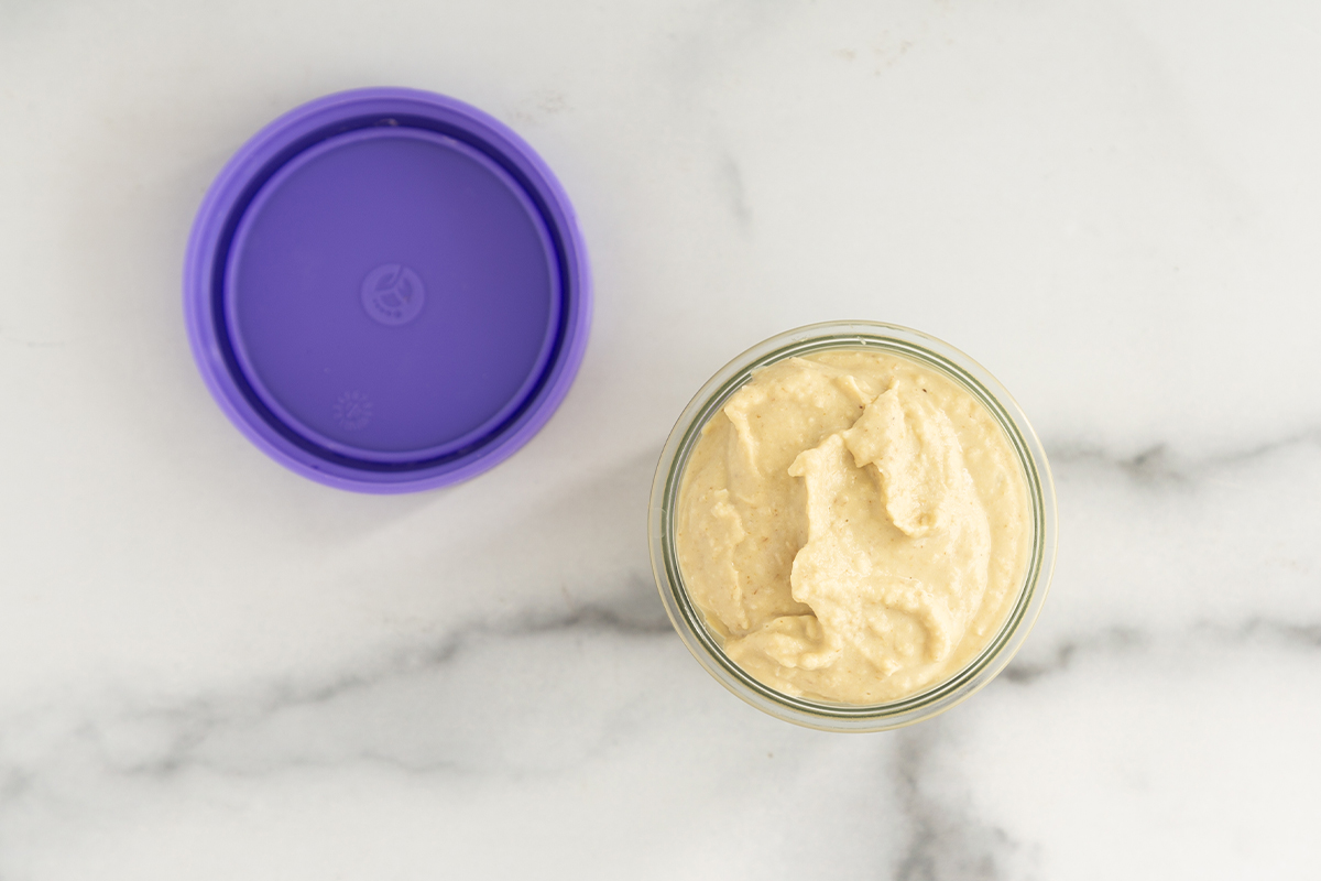 Baby hummus in glass jar with purple lid on side.