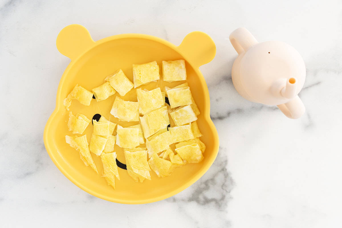 Baby omelette on yellow baby plate cut into bite sized pieces.