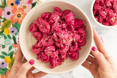 Hands holding bowl of beet pasta sauce.