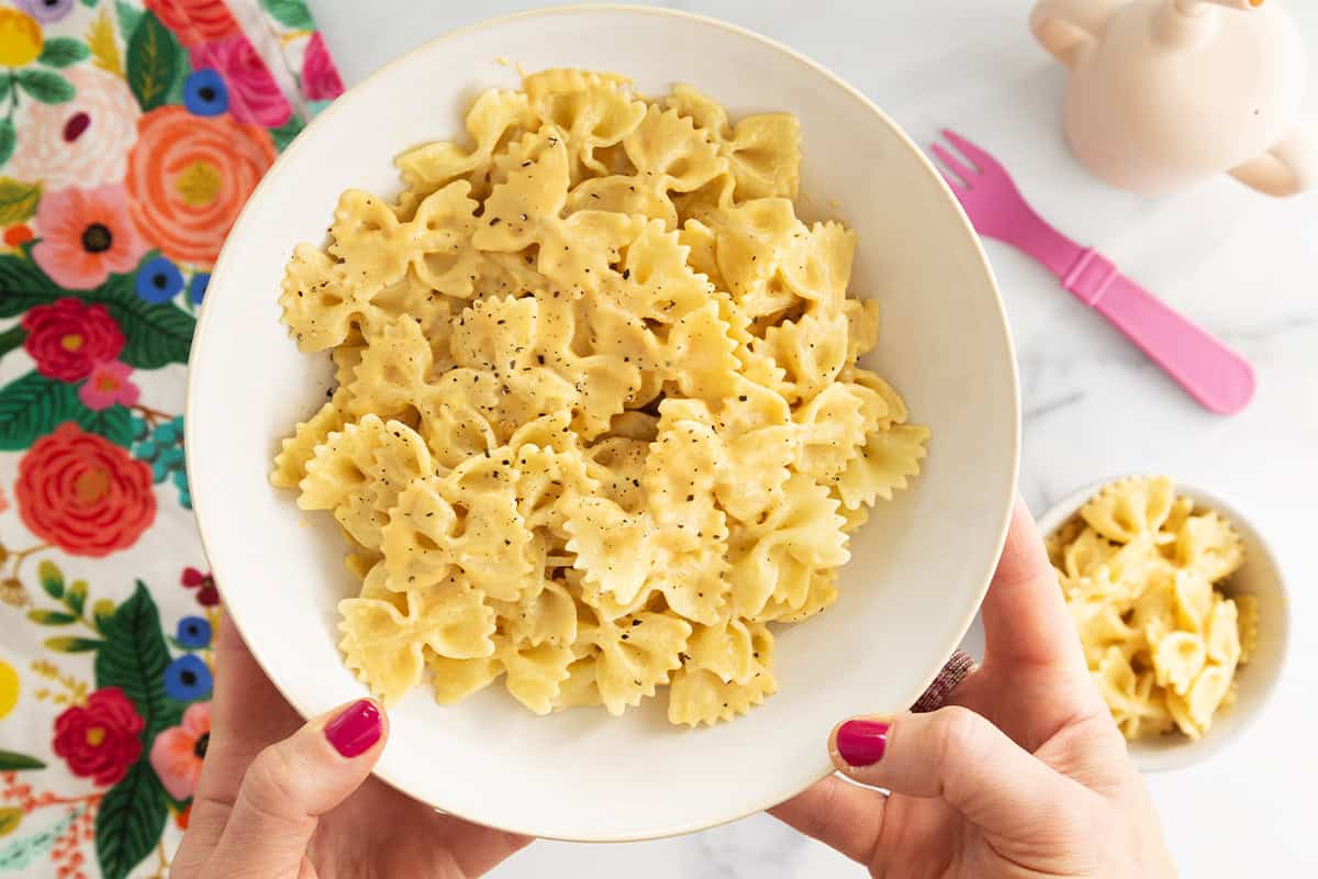 Butternut pasta sauce in white bowl with hands holding bowl.